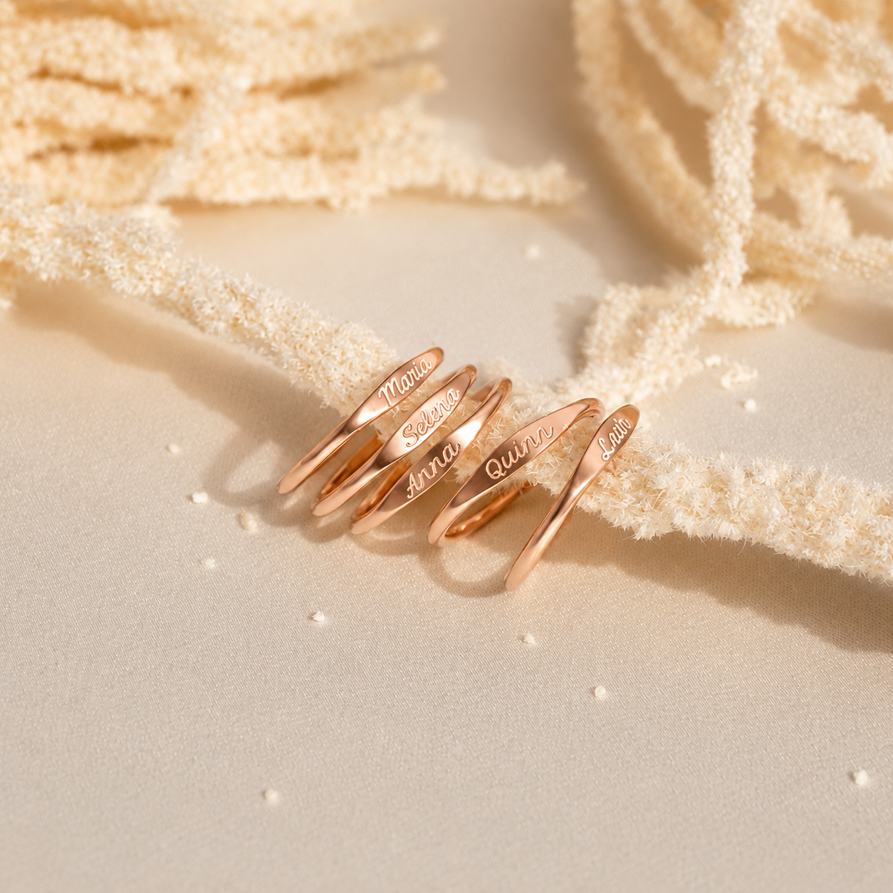 Rose gold rings with engraved names on a textured beige surface